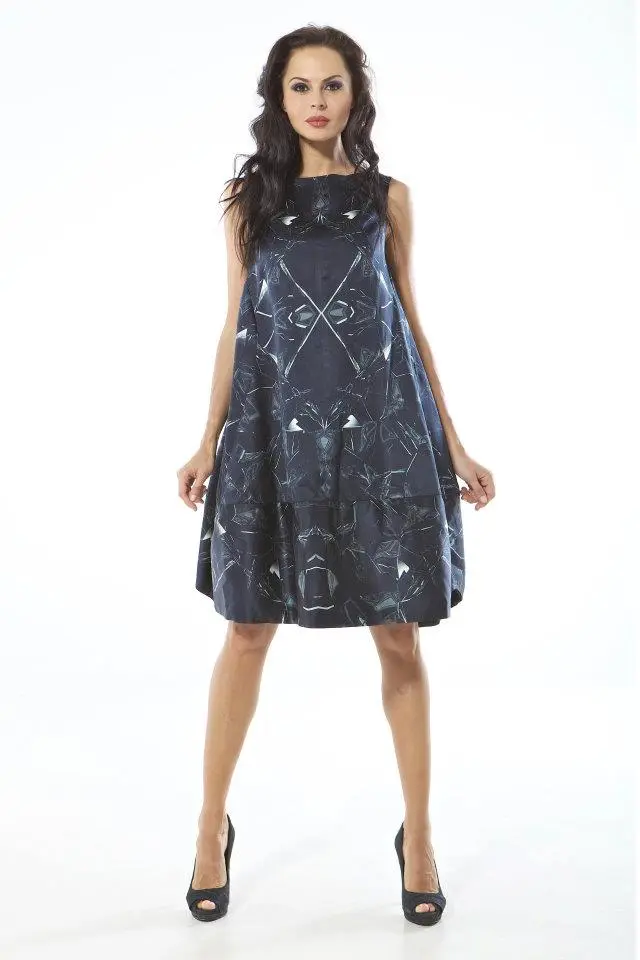 Model wearing a knee-length black dress with a reflective broken glass print in greys, cut in barrel-shaped panels inspired by Vionnet.
